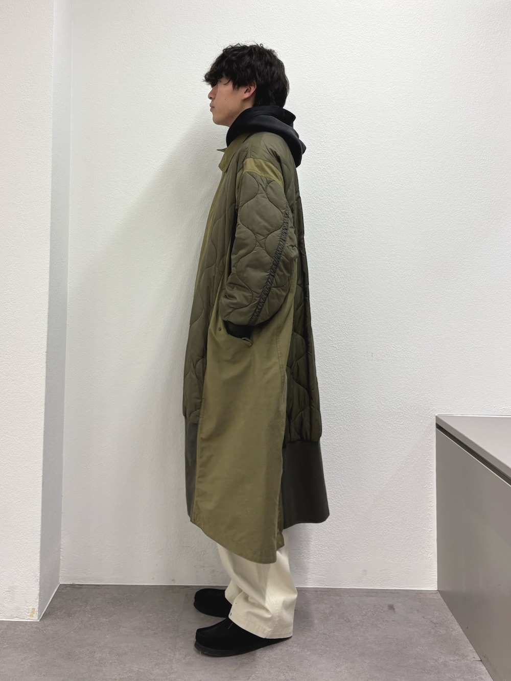 ブラック系のパーカー、ホワイト系のチノパンツ、グリーン系のモッズコートを着用したメンズの冬コーディネートの2枚目の写真