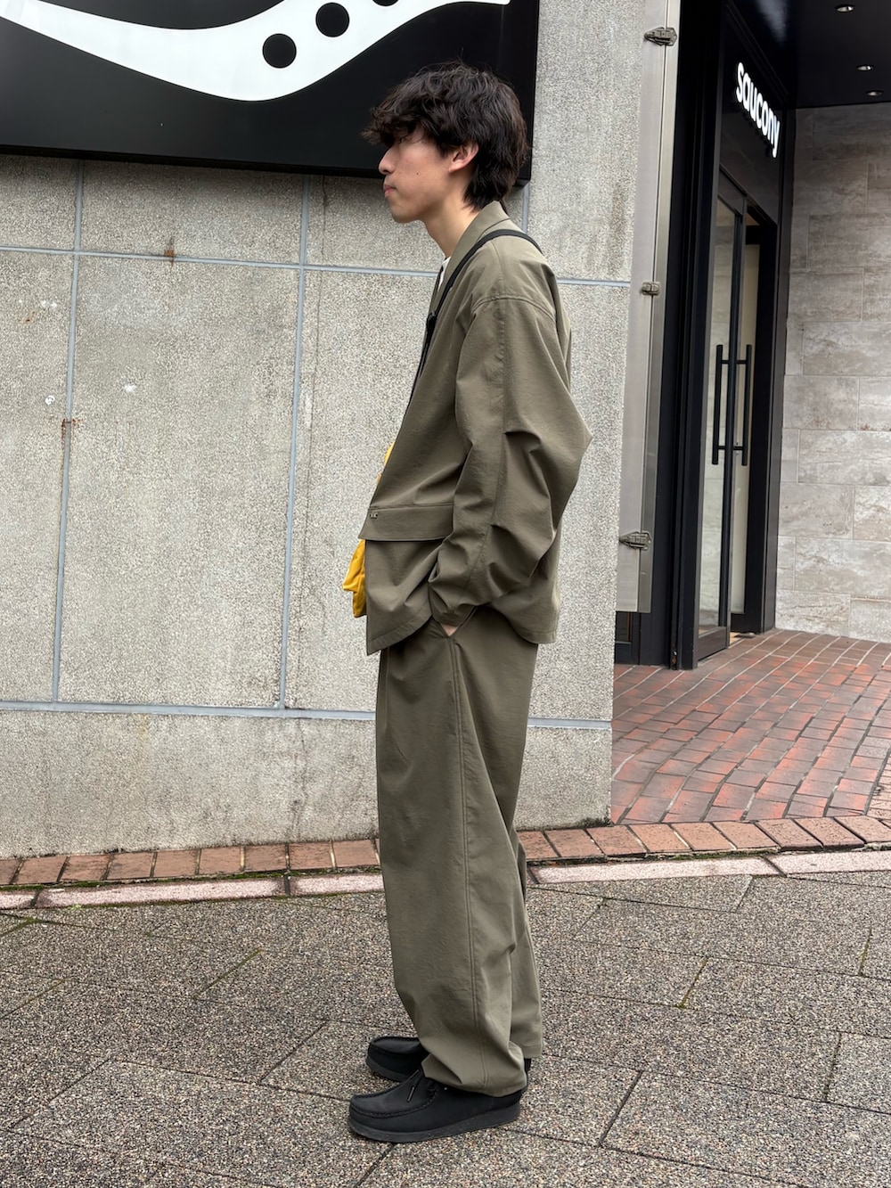 イエロー系のショルダーバッグ、グリーン系のテーラードジャケット、グリーン系のスラックスを着用したメンズの春コーディネートの2枚目の写真