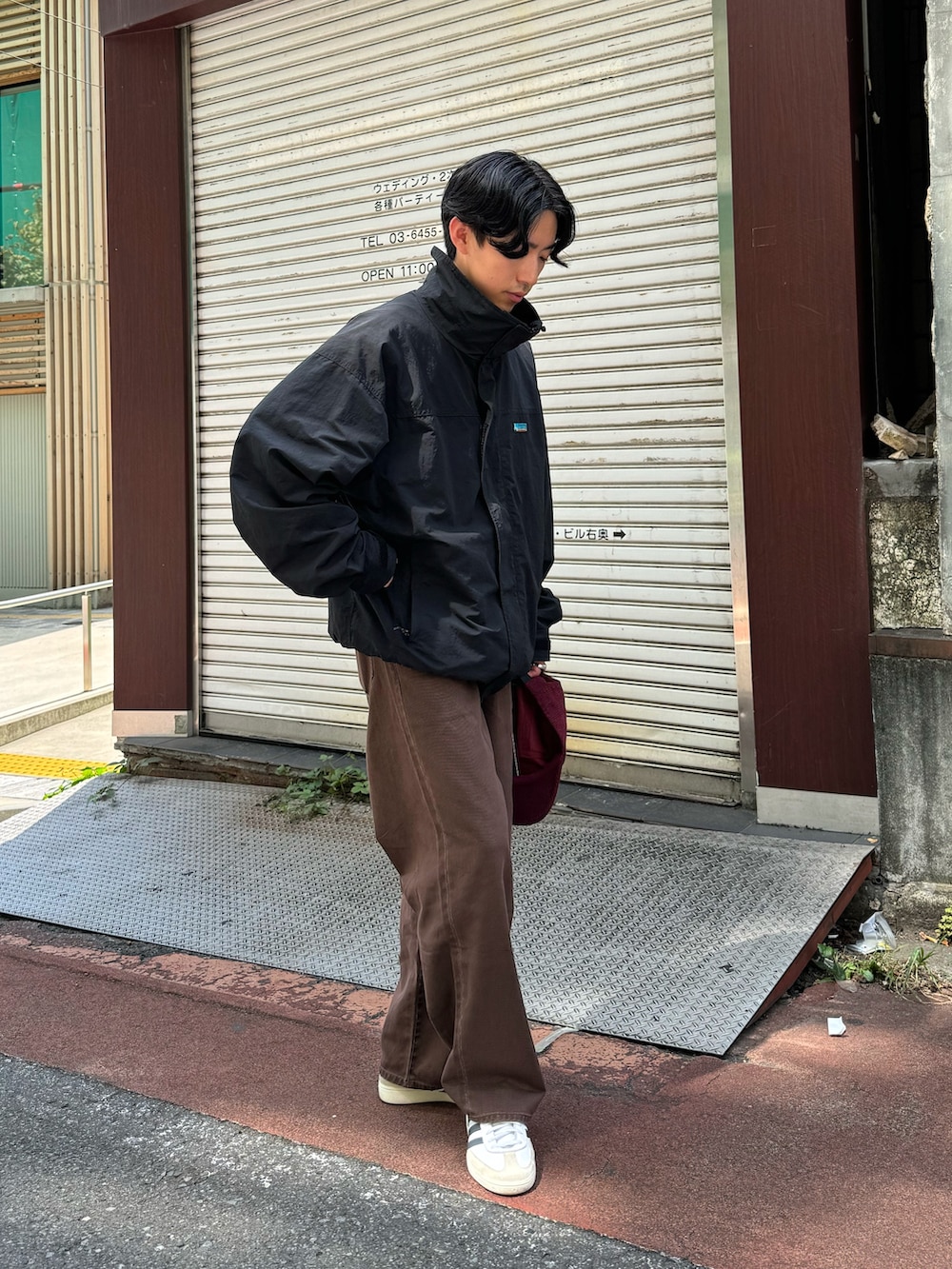 ブラウン系のデニムパンツ、ブラック系のナイロンジャケット、レッド系のキャップを着用したメンズの秋コーディネートの2枚目の写真