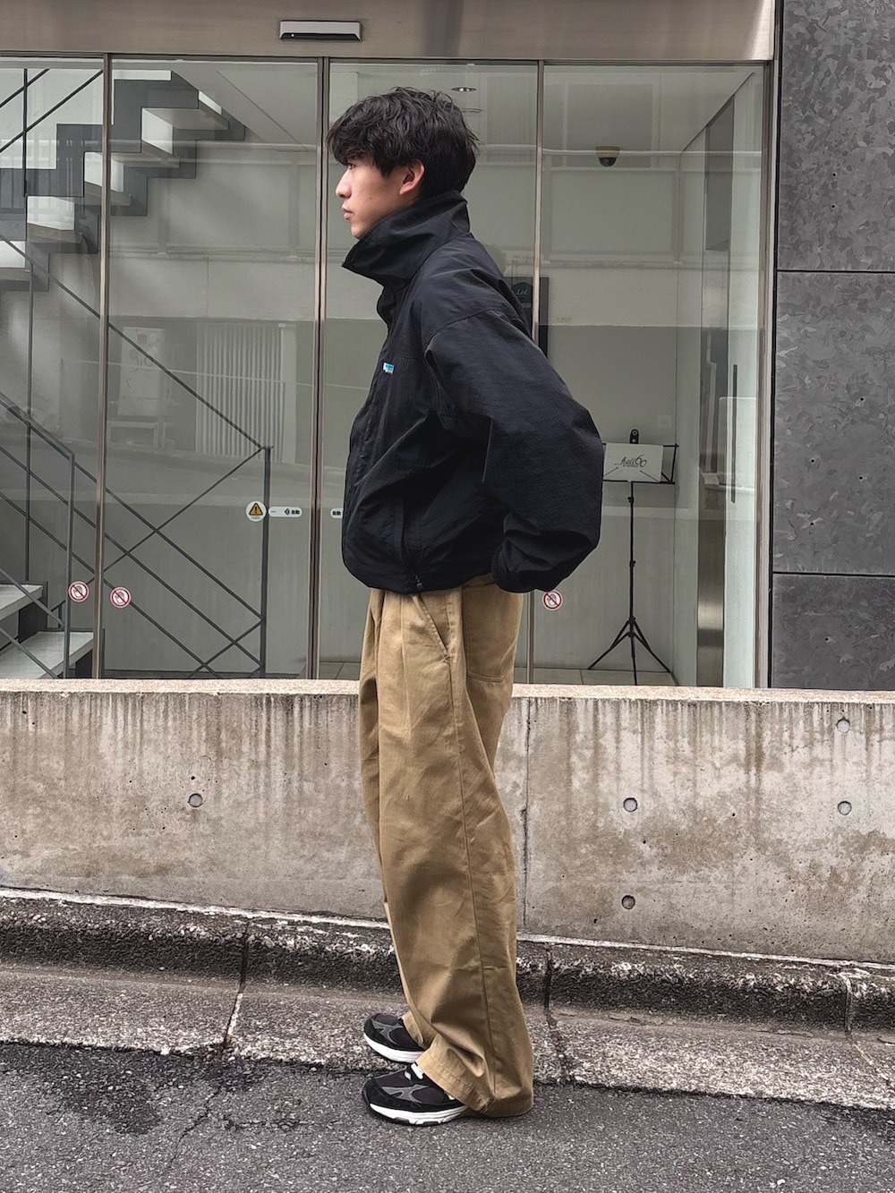 ブラック系のナイロンジャケット、ベージュ系のデニムパンツを着用したメンズの春コーディネートの2枚目の写真