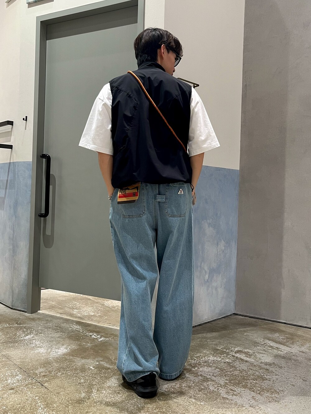 ブラック系のスニーカー、ブルー系のデニムパンツ、ブラック系のベストを着用したメンズの春コーディネートの3枚目の写真