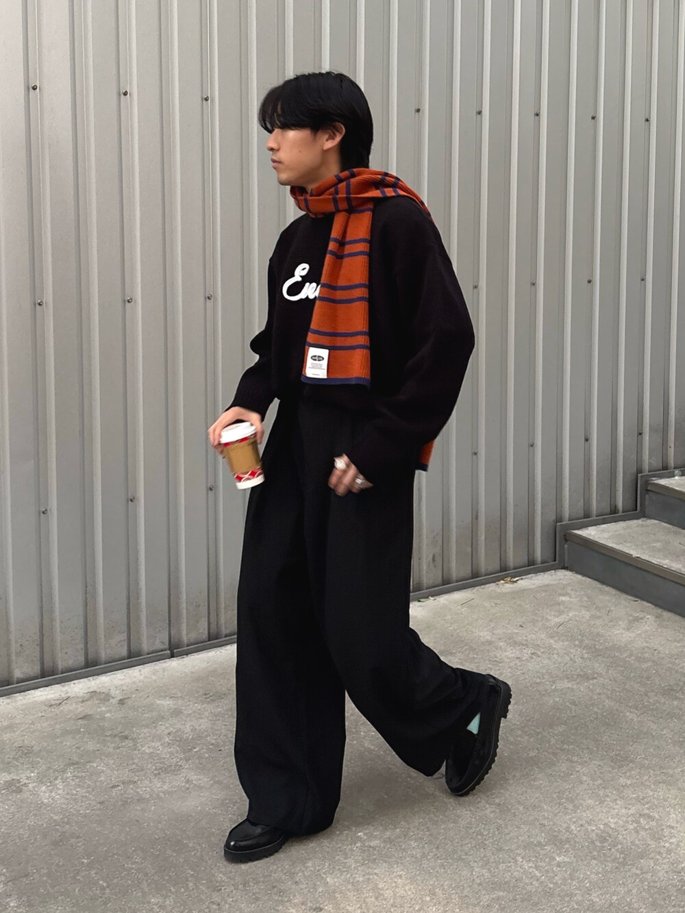 ブラック系のスラックス、ブラック系のニット/セーター、オレンジ系のマフラーを着用したメンズの冬コーディネートの2枚目の写真