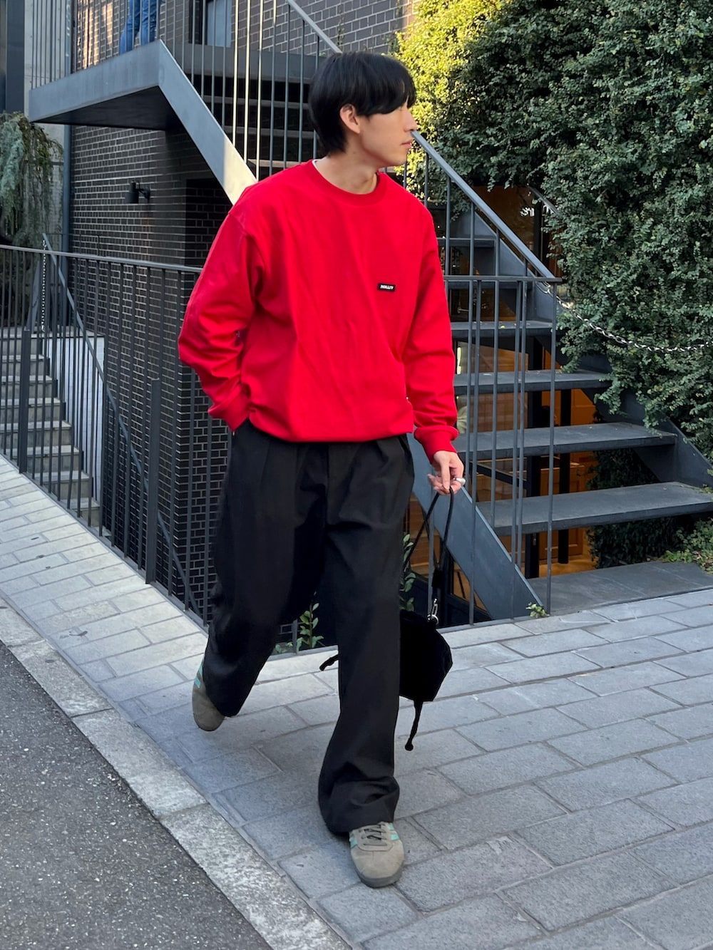 レッド系のTシャツ/カットソー、ブラック系のスラックス、グレー系のスニーカーを着用したメンズの秋コーディネートの2枚目の写真