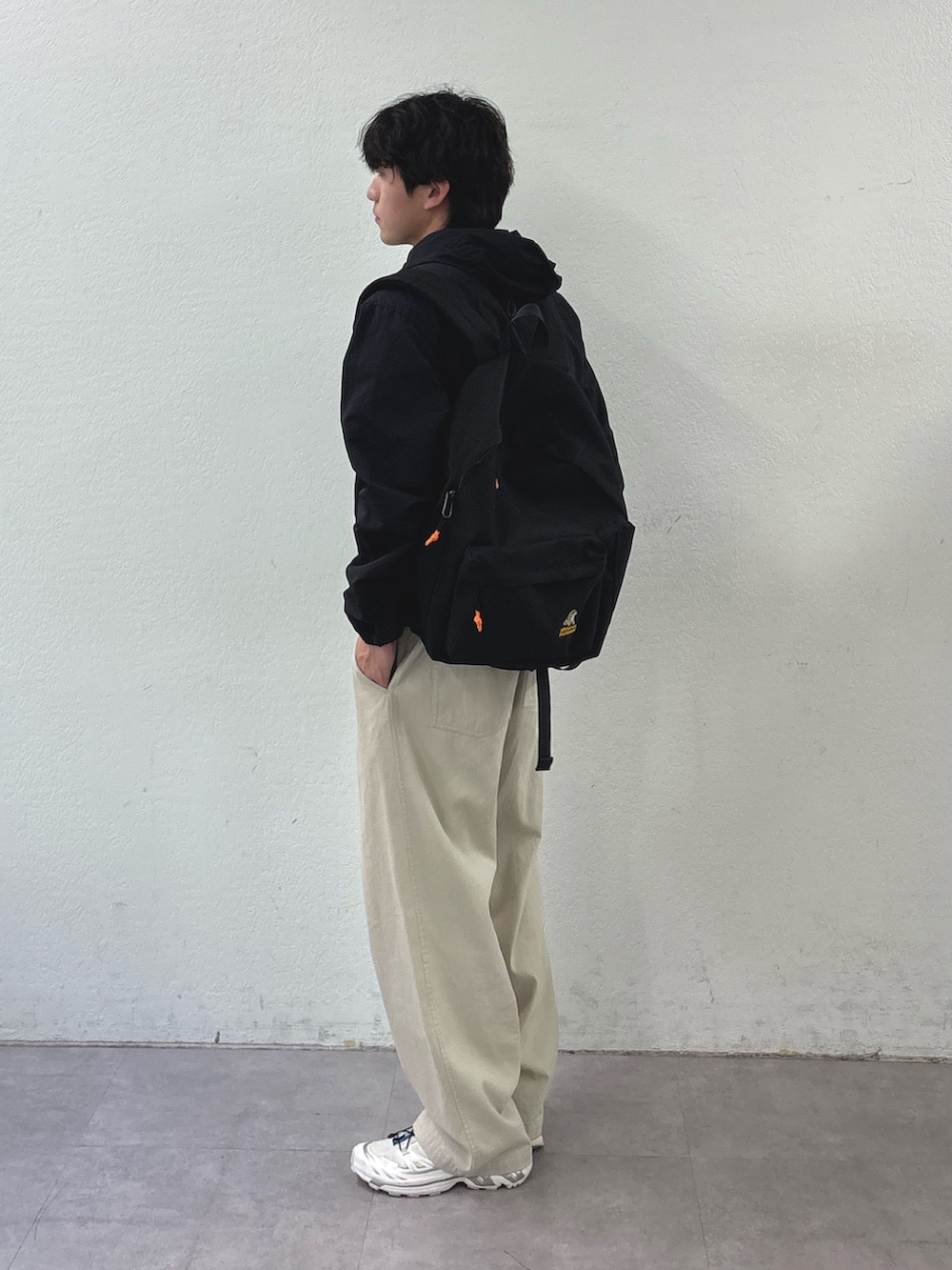 ブラック系のマウンテンパーカー、ブラック系のバックパック/リュック、ホワイト系のチノパンツを着用したメンズの春コーディネートの2枚目の写真