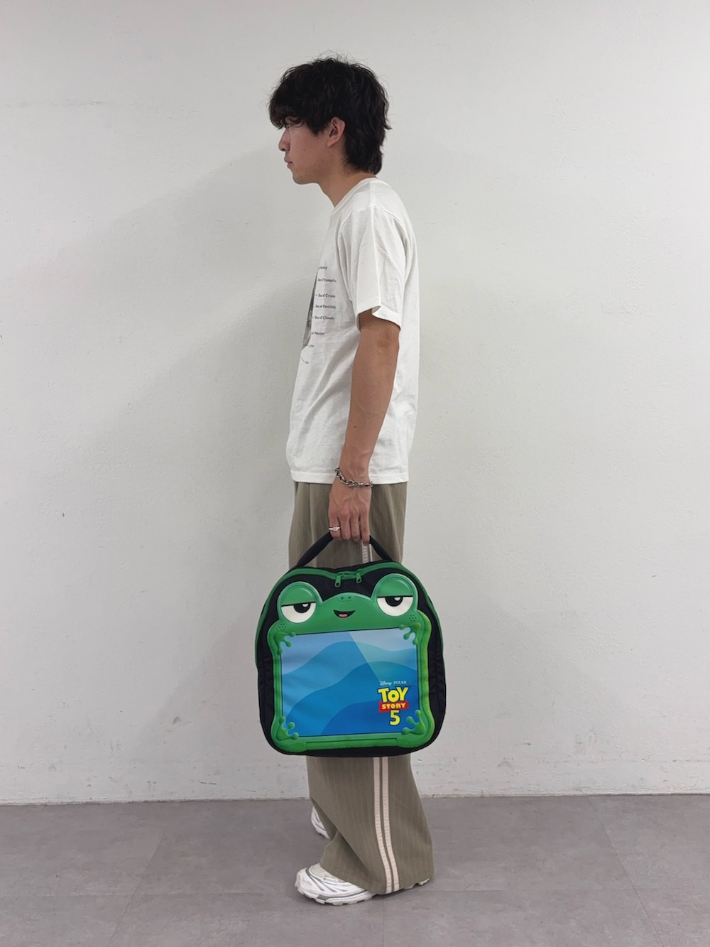 ホワイト系のTシャツ/カットソー、ベージュ系のスラックス、ブラック系のPC・タブレットケースを着用したメンズの夏コーディネートの2枚目の写真