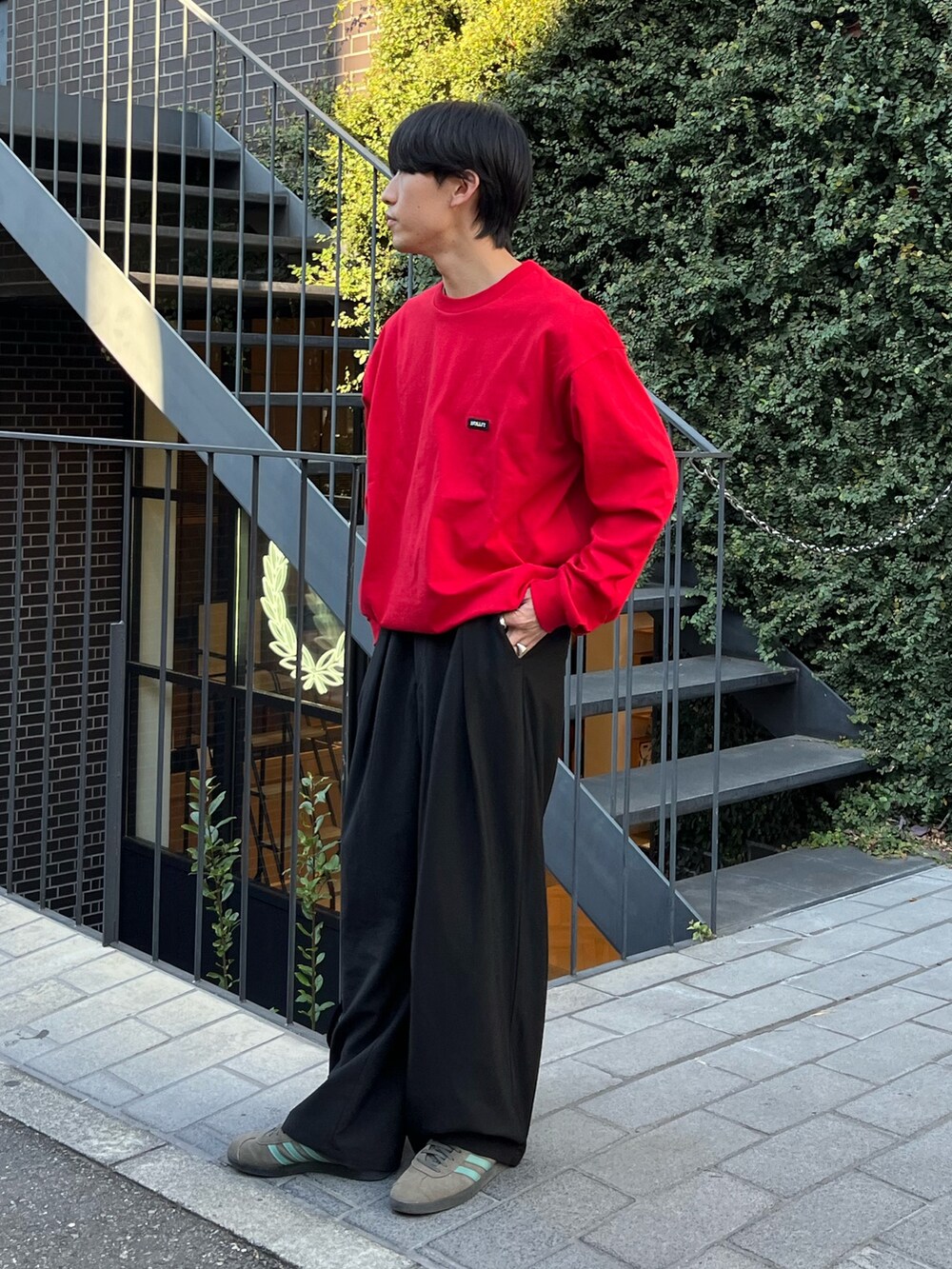 レッド系のTシャツ/カットソー、ブラック系のダウンベスト、ブラック系のスラックスを着用したメンズの秋コーディネートの2枚目の写真