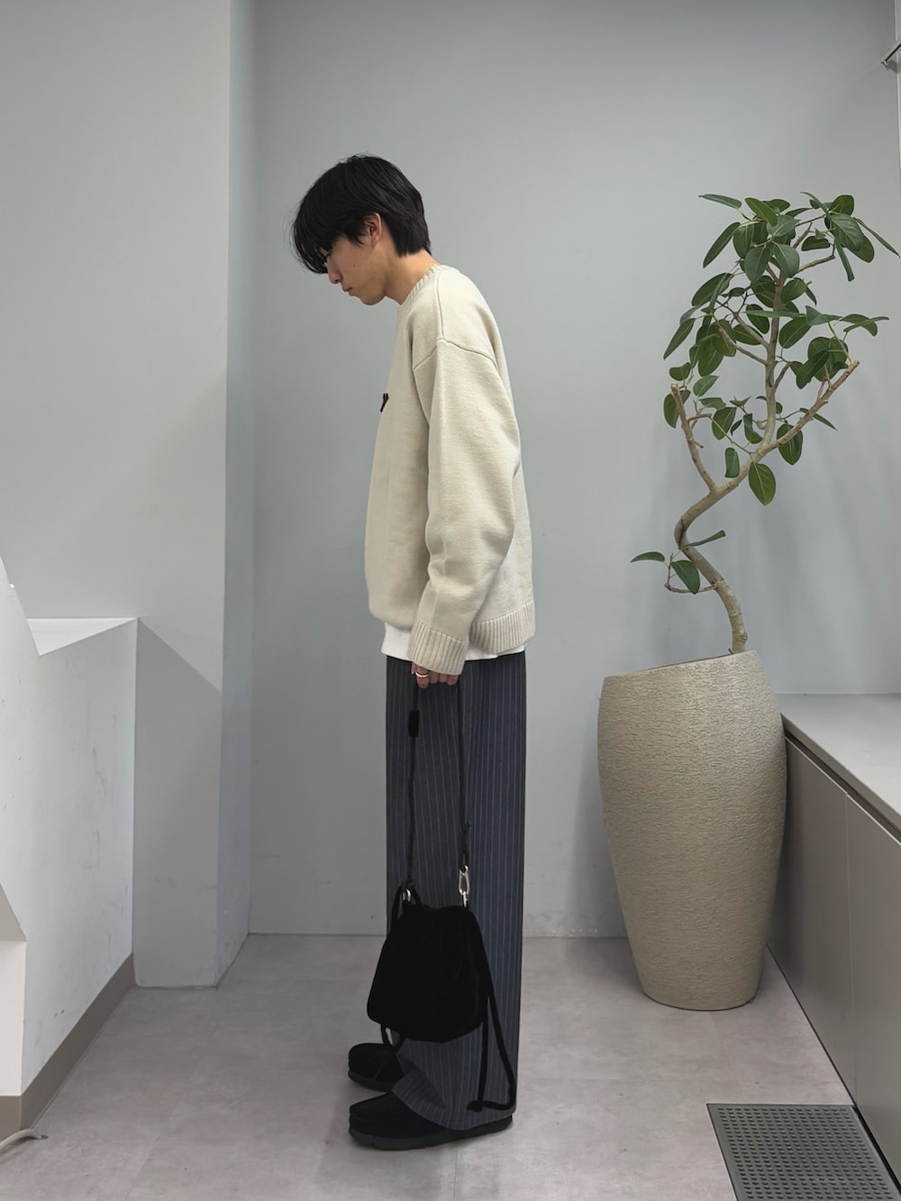 ブラック系のショルダーバッグ、グレー系のスラックス、ホワイト系のニット/セーターを着用したメンズの春コーディネートの2枚目の写真