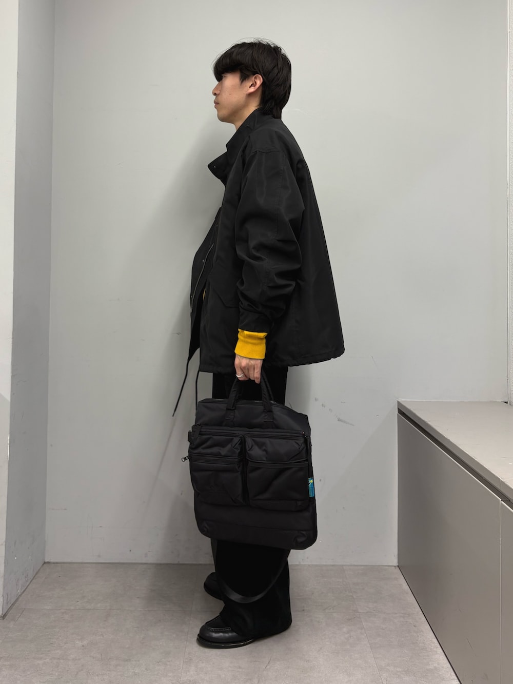 ブラック系のモッズコート、イエロー系のニット/セーター、ブラック系のショルダーバッグを着用したメンズの冬コーディネートの2枚目の写真