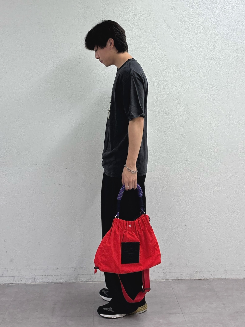 ブラック系のTシャツ/カットソー、ブラック系のスラックス、レッド系のトートバッグを着用したメンズの夏コーディネートの2枚目の写真