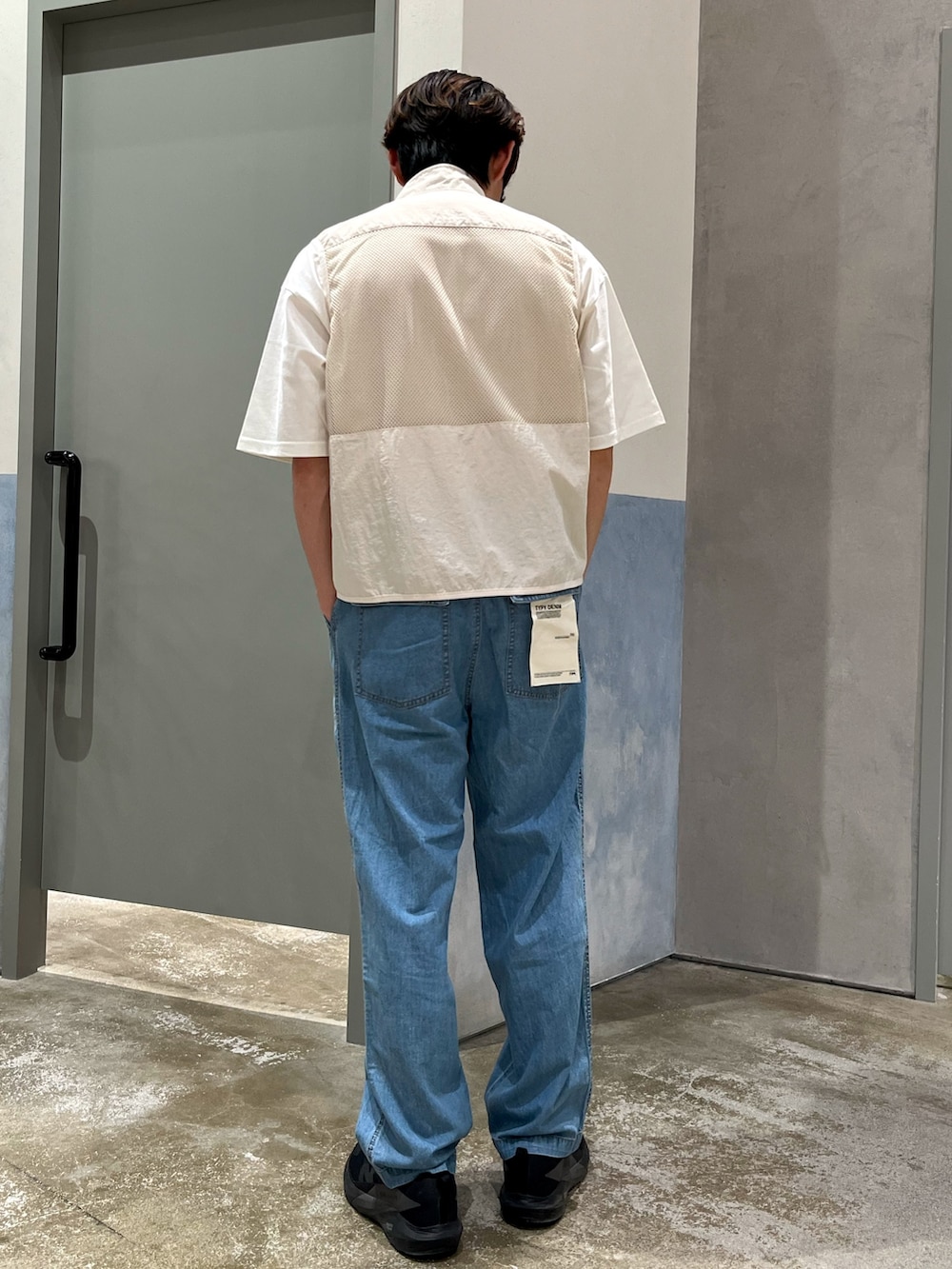 ブラック系のスニーカー、ブルー系のデニムパンツ、ホワイト系のベストを着用したメンズの夏コーディネートの3枚目の写真