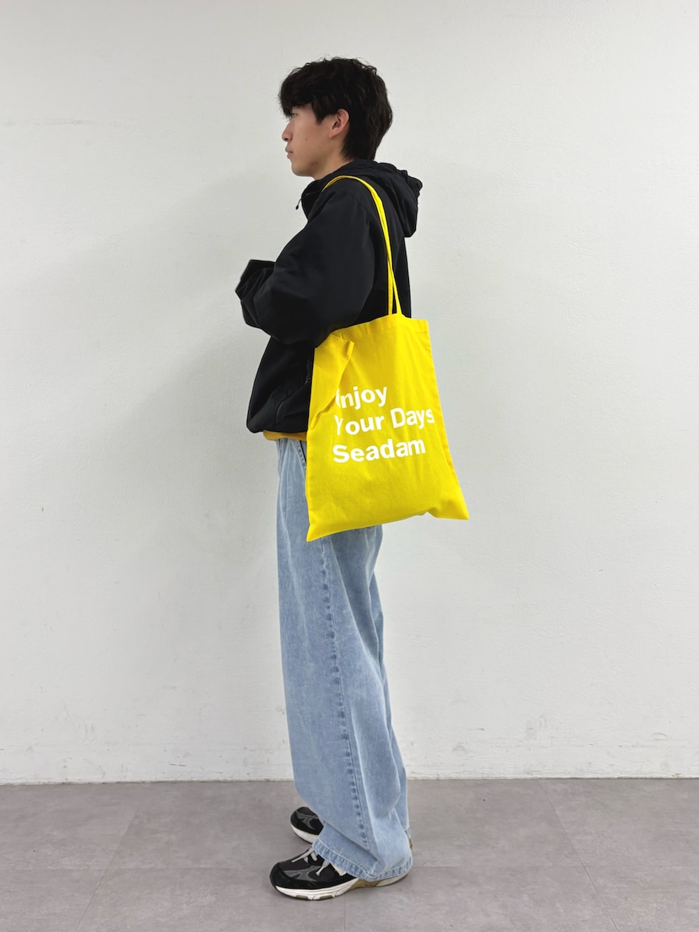 ブラック系のパーカー、イエロー系のトートバッグ、ブルー系のデニムパンツを着用したメンズの春コーディネートの2枚目の写真