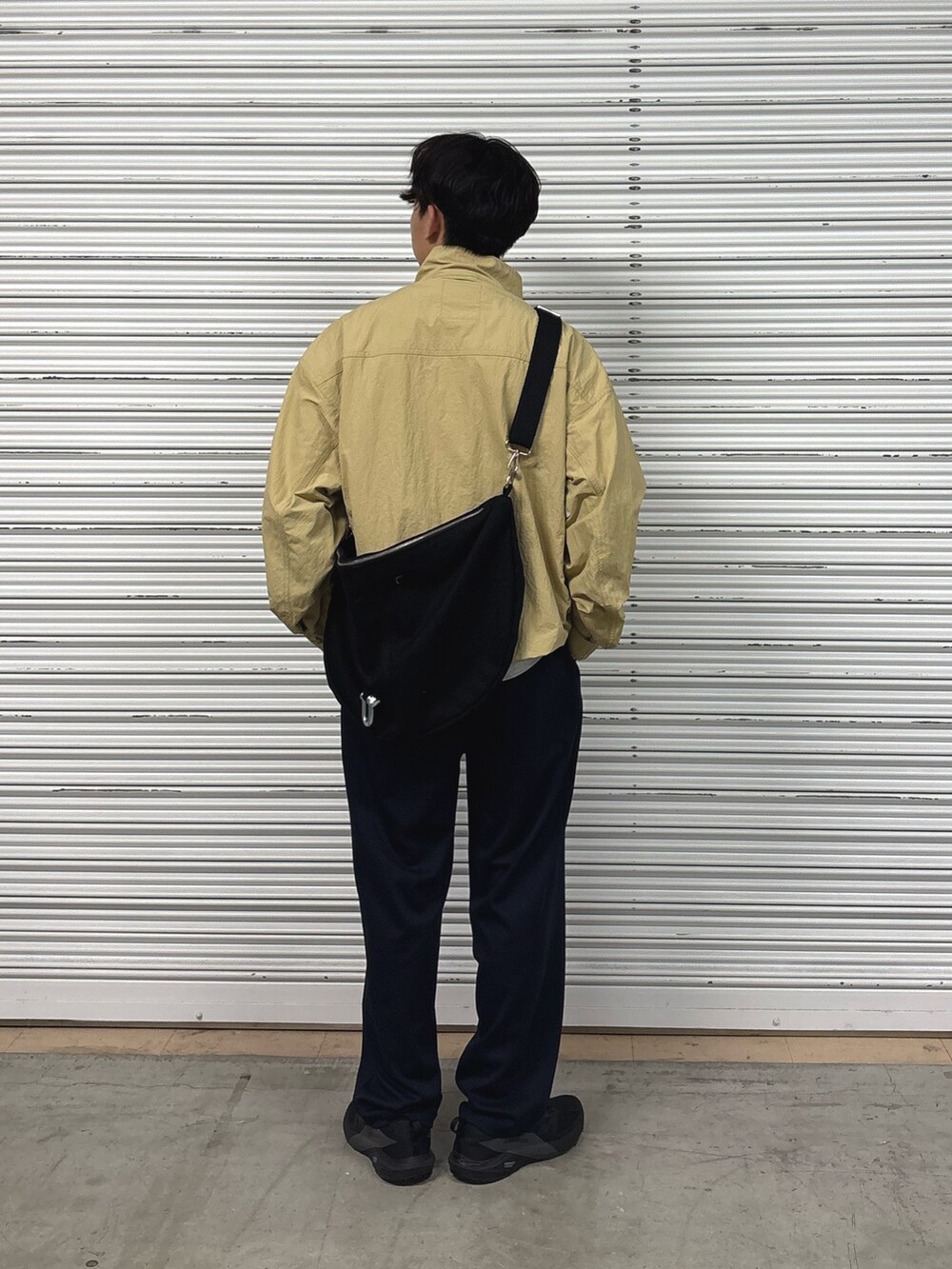 ベージュ系のナイロンジャケット、ブラック系のショルダーバッグ、ブラック系のスラックスを着用したメンズの夏コーディネートの3枚目の写真