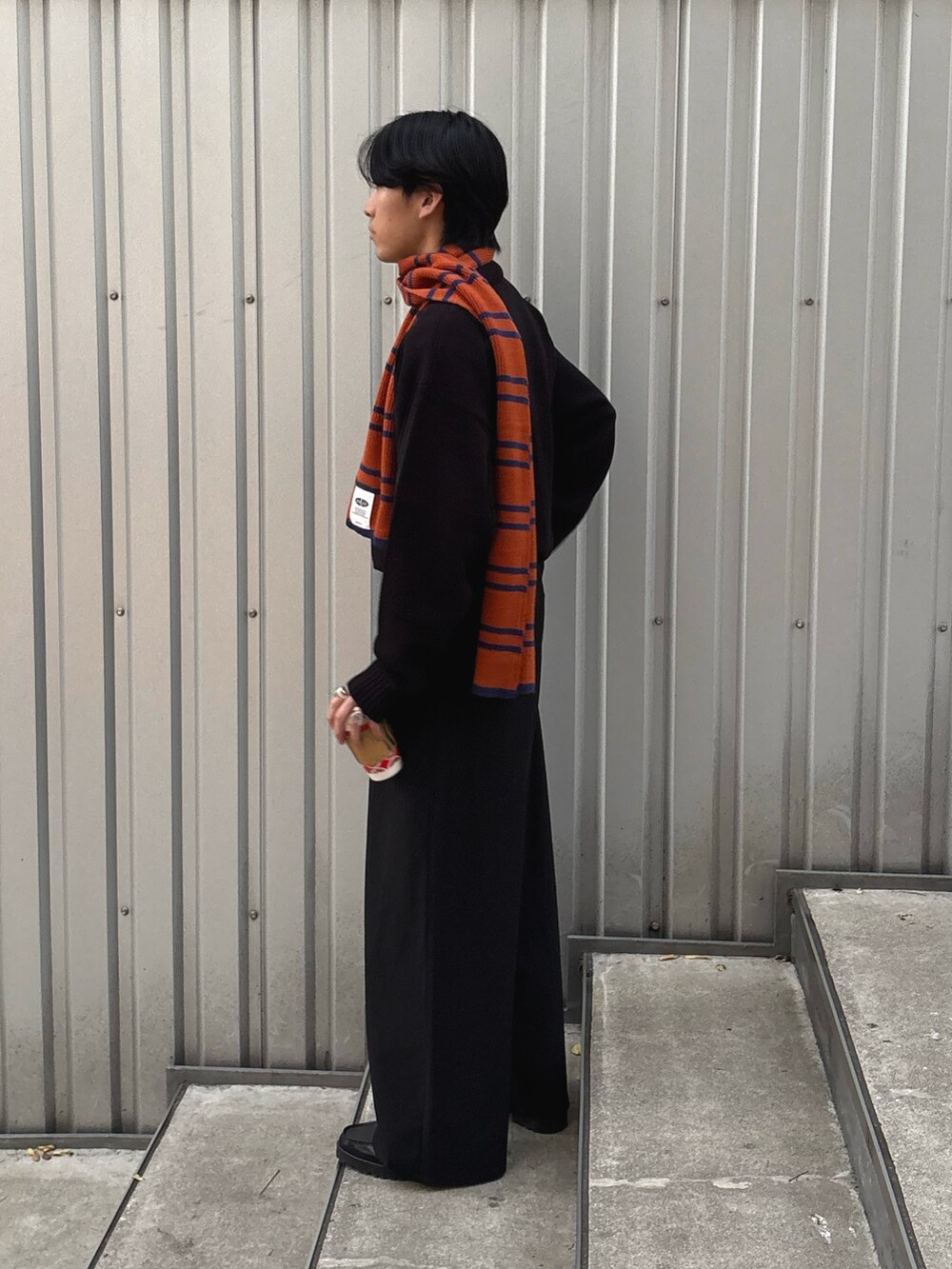 ブラック系のスラックス、ブラック系のニット/セーター、オレンジ系のマフラーを着用したメンズの冬コーディネートの3枚目の写真