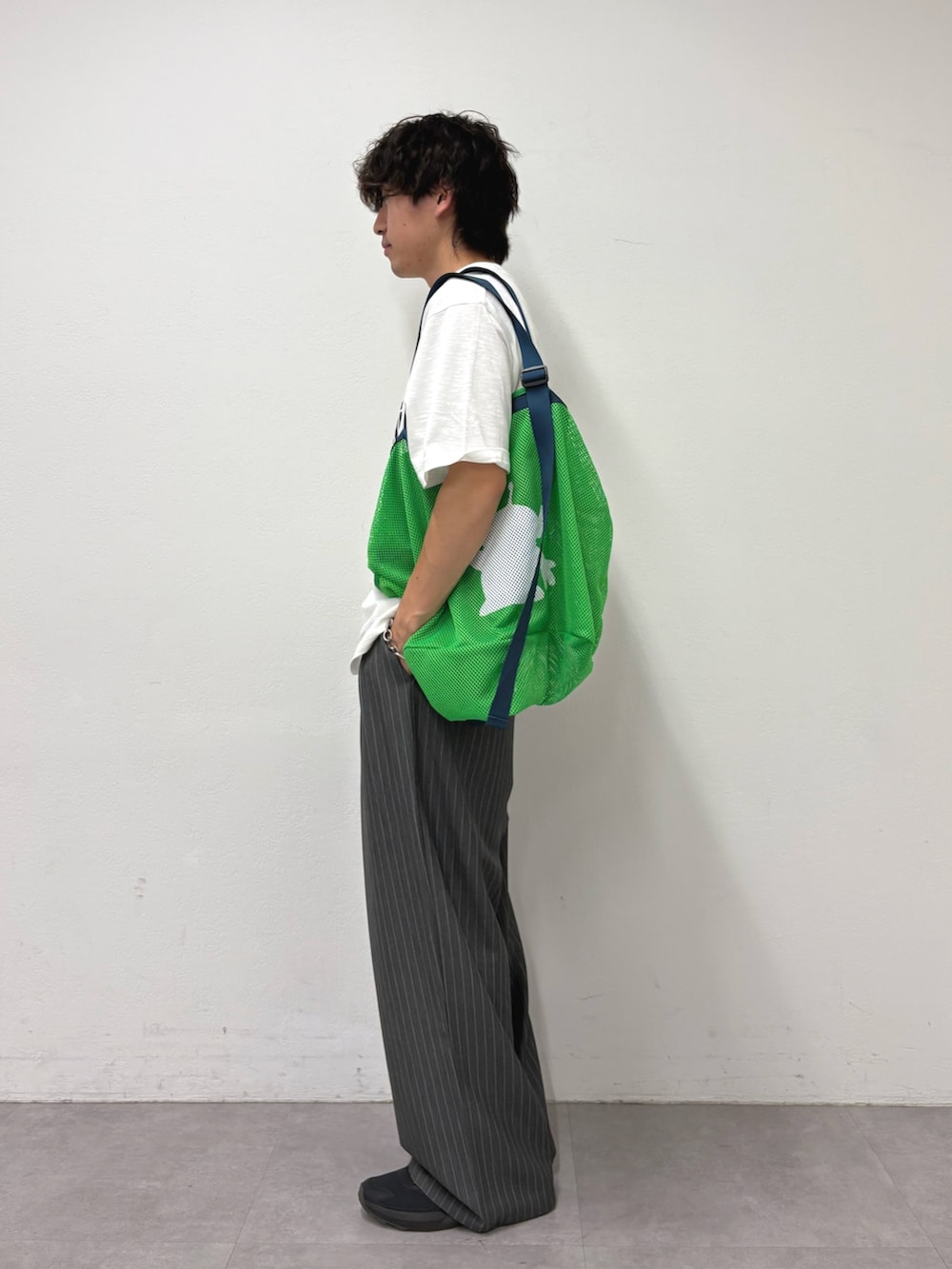 ホワイト系のTシャツ/カットソー、グリーン系のトートバッグ、グレー系のスラックスを着用したメンズの夏コーディネートの2枚目の写真