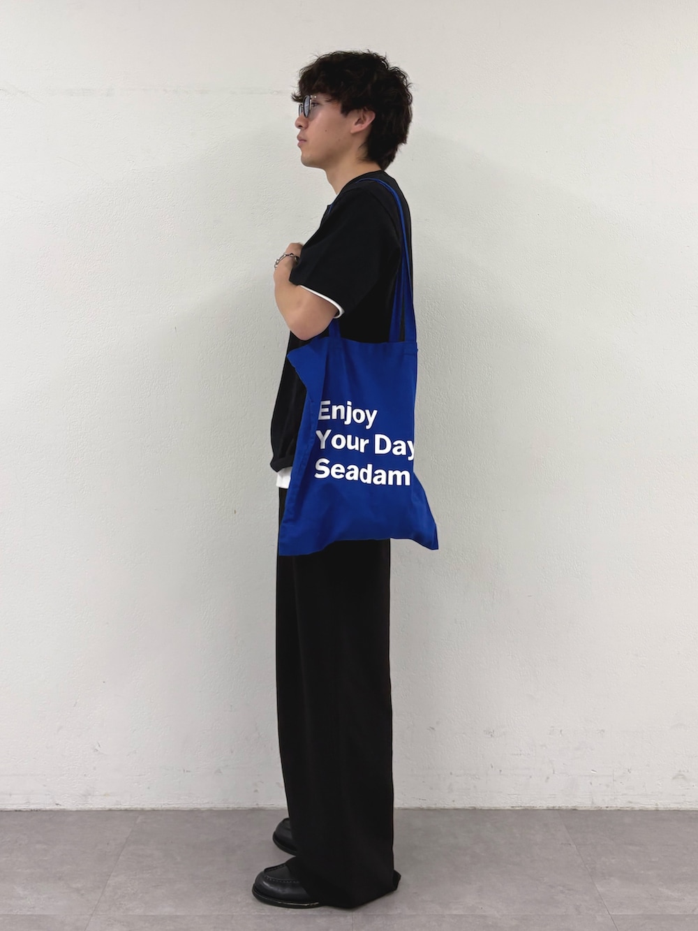 ブラック系のTシャツ/カットソー、ブルー系のトートバッグ、ブラック系のスラックスを着用したメンズの春コーディネートの2枚目の写真