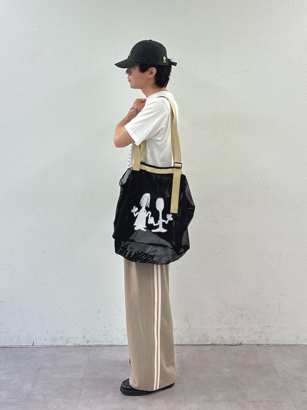 ブラック系のトートバッグ、ホワイト系のTシャツ/カットソー、ベージュ系のスラックスを着用したメンズの夏コーディネートの2枚目の写真