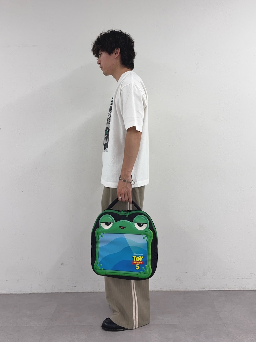ホワイト系のTシャツ/カットソー、ベージュ系のスラックス、ブラック系のPC・タブレットケースを着用したメンズの夏コーディネートの2枚目の写真