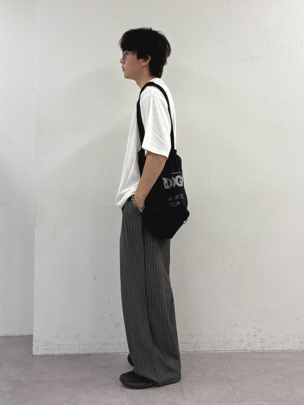 ホワイト系のTシャツ/カットソー、ブラック系のトートバッグ、グレー系のスラックスを着用したメンズの夏コーディネートの2枚目の写真