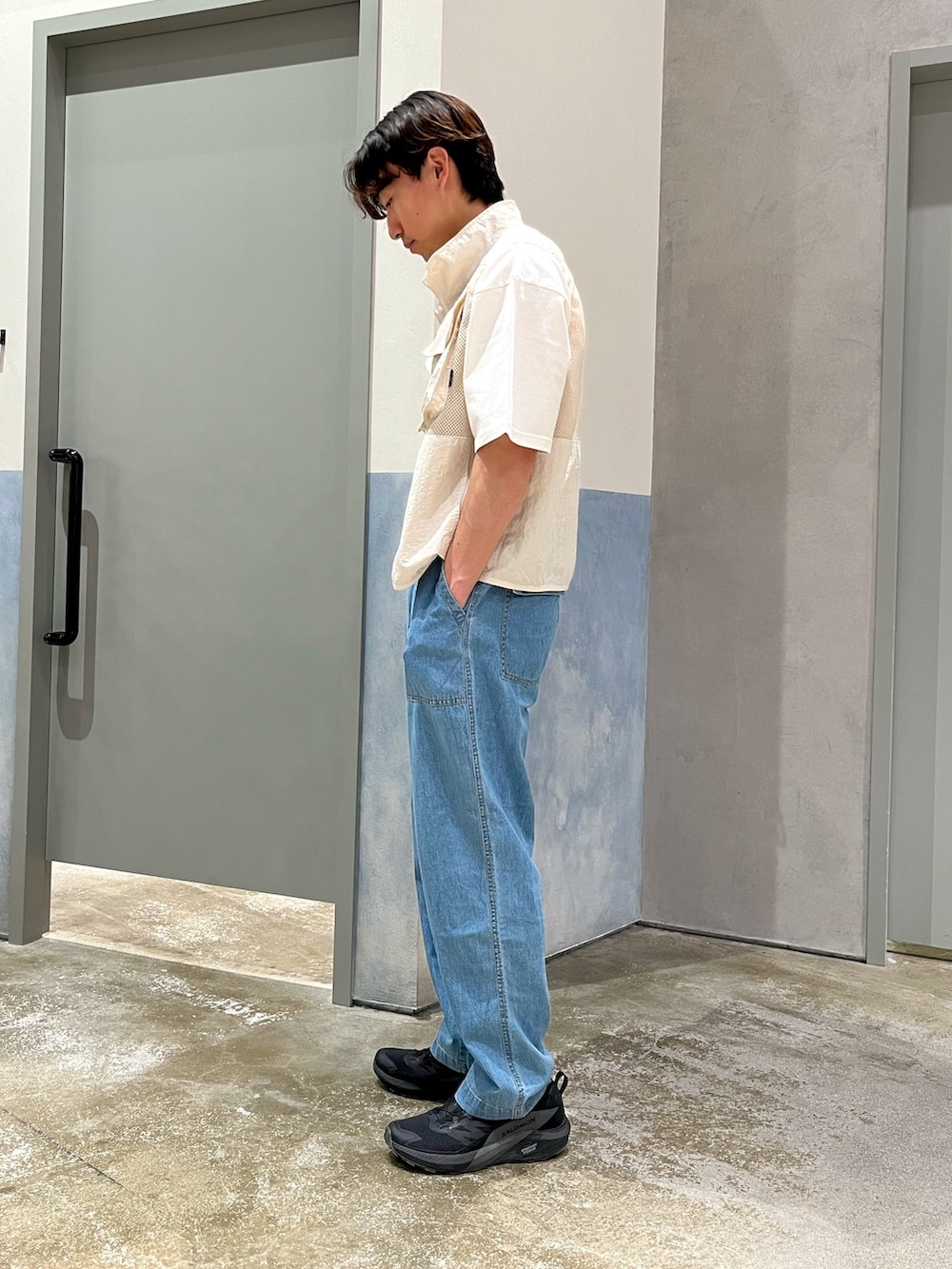 ブラック系のスニーカー、ブルー系のデニムパンツ、ホワイト系のベストを着用したメンズの夏コーディネートの2枚目の写真