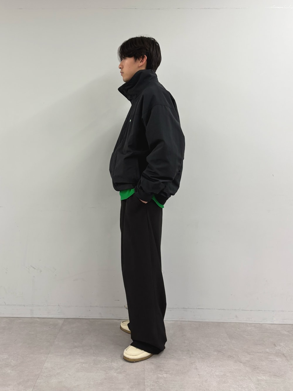 ブラック系のナイロンジャケット、グリーン系のニット/セーター、ブラック系のスラックスを着用したメンズの秋コーディネートの2枚目の写真