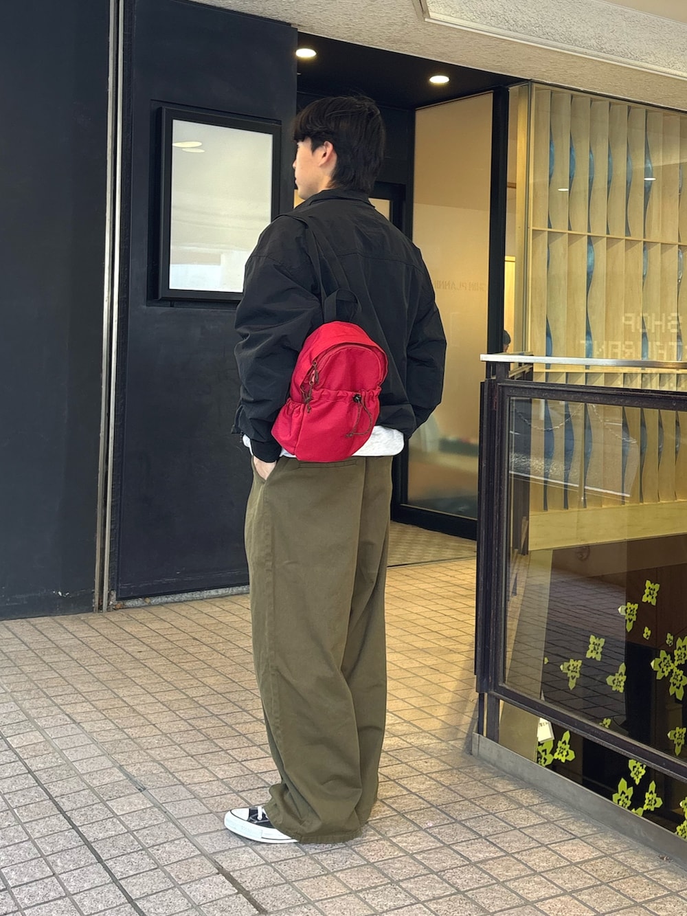 グリーン系のスラックス、ブラック系のナイロンジャケット、レッド系のバックパック/リュックを着用したメンズの春コーディネートの2枚目の写真