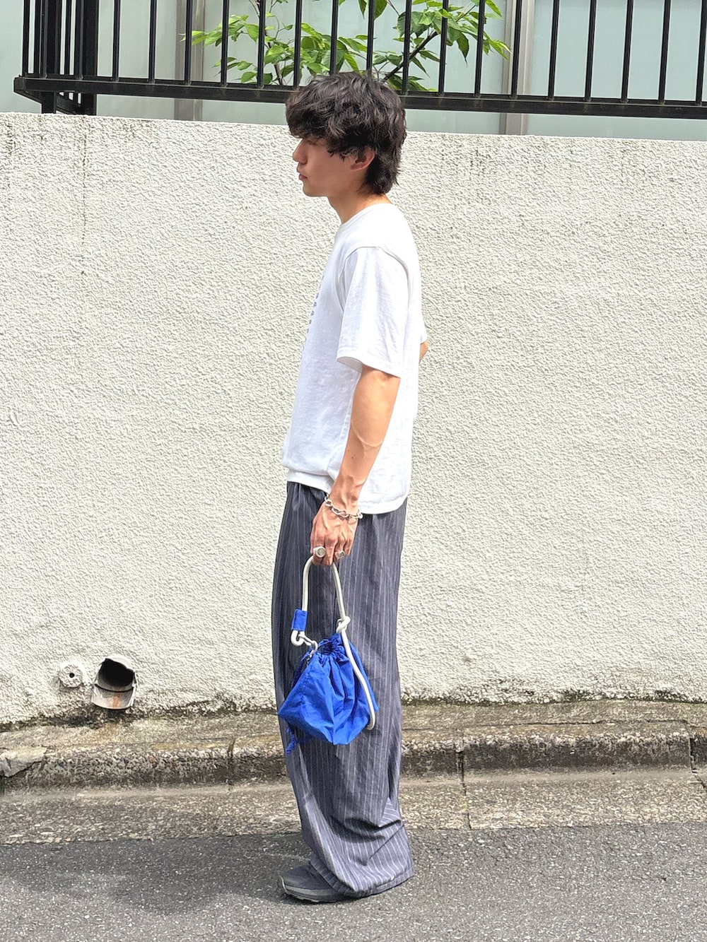 ホワイト系のTシャツ/カットソー、グレー系のスラックス、ブルー系のショルダーバッグを着用したメンズの夏コーディネートの2枚目の写真