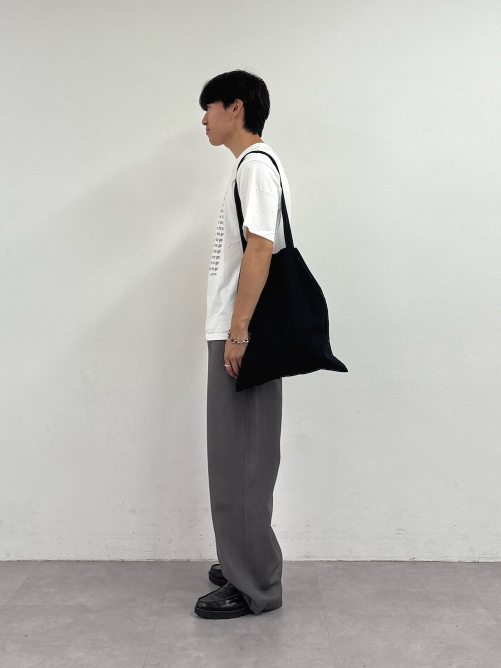 ホワイト系のTシャツ/カットソー、ブラック系のトートバッグ、グレー系のスラックスを着用したメンズの夏コーディネートの2枚目の写真