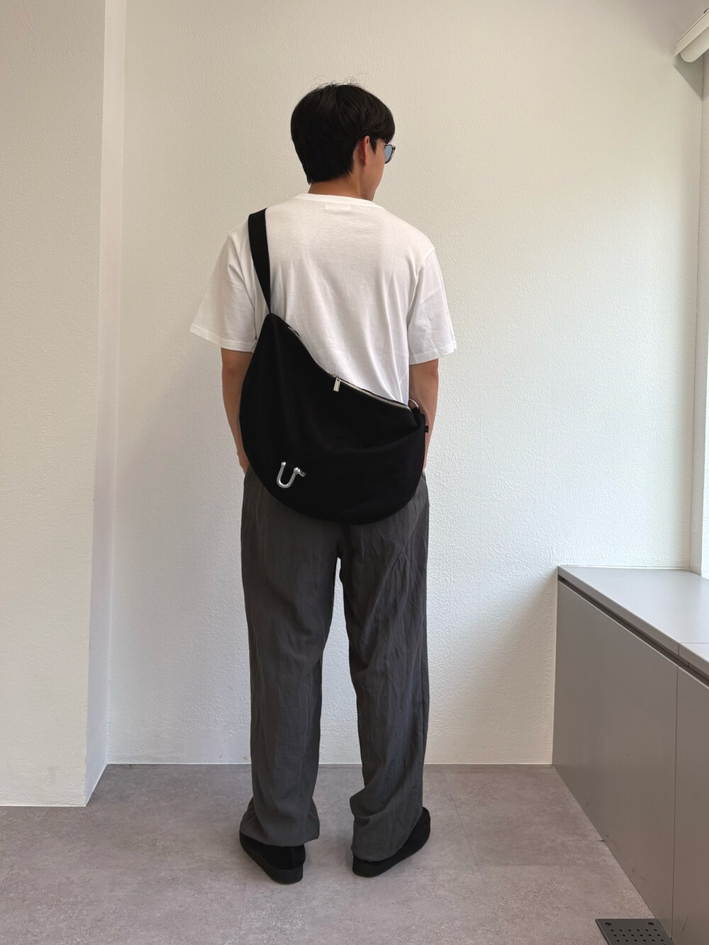 ホワイト系のTシャツ/カットソー、ブラック系のショルダーバッグ、グレー系のスラックスを着用したメンズの夏コーディネートの2枚目の写真