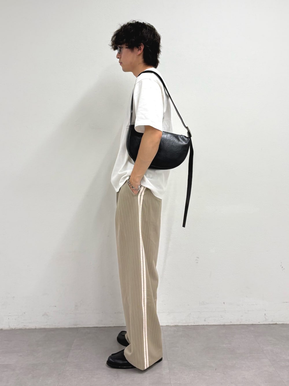 ホワイト系のTシャツ/カットソー、ブラック系のショルダーバッグ、ベージュ系のスラックスを着用したメンズの夏コーディネートの2枚目の写真