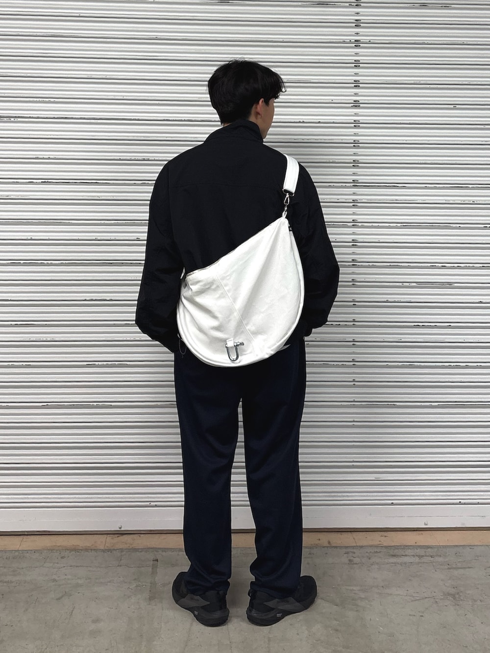 ブラック系のナイロンジャケット、ブルー系のスラックス、ホワイト系のショルダーバッグを着用したメンズの春コーディネートの3枚目の写真