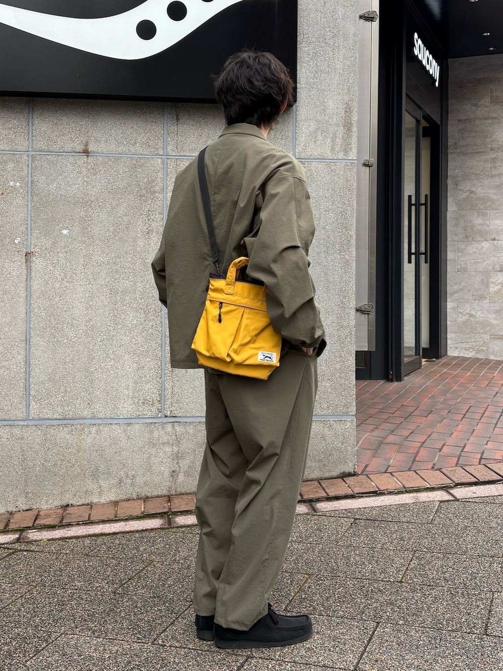 イエロー系のショルダーバッグ、グリーン系のテーラードジャケット、グリーン系のスラックスを着用したメンズの春コーディネートの3枚目の写真