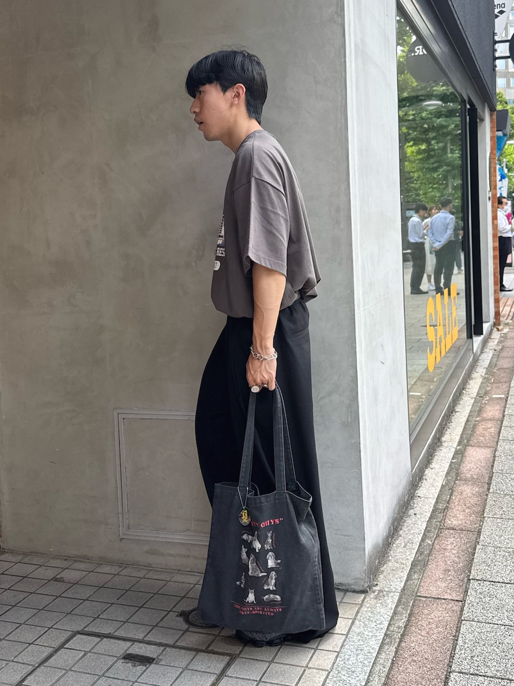 グレー系のTシャツ/カットソー、ブラック系のスラックス、ブラック系のトートバッグを着用したメンズの夏コーディネートの2枚目の写真