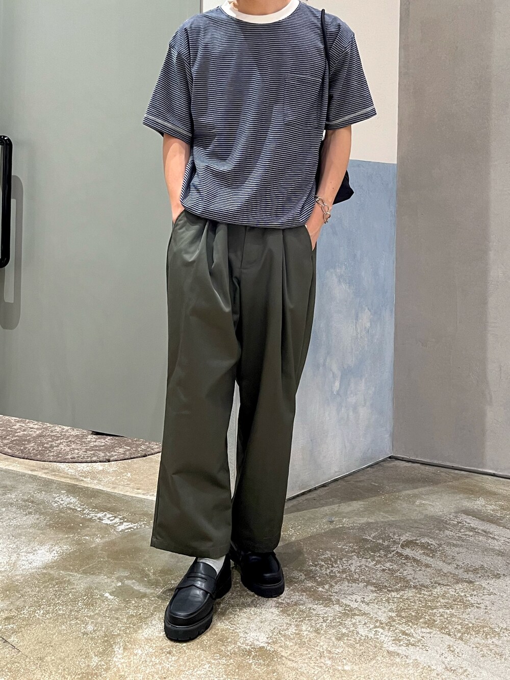 グリーン系のチノパンツ、ブルー系のTシャツ/カットソー、ブラック系のショルダーバッグを着用したメンズの夏コーディネートの3枚目の写真