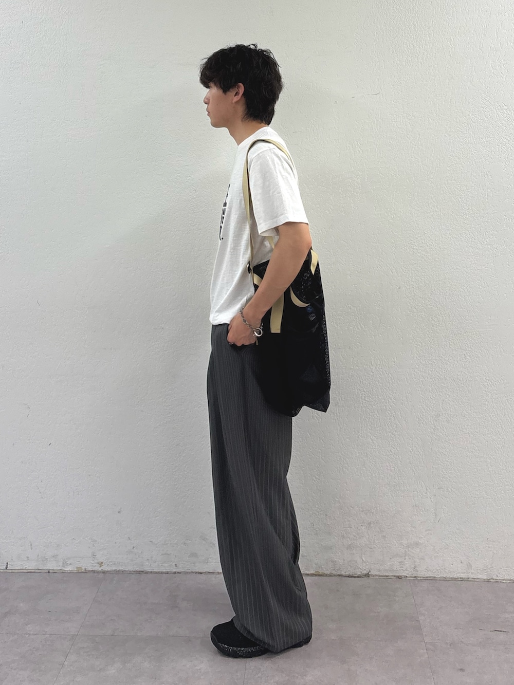 ホワイト系のTシャツ/カットソー、ブラック系のトートバッグ、グレー系のスラックスを着用したメンズの春コーディネートの2枚目の写真