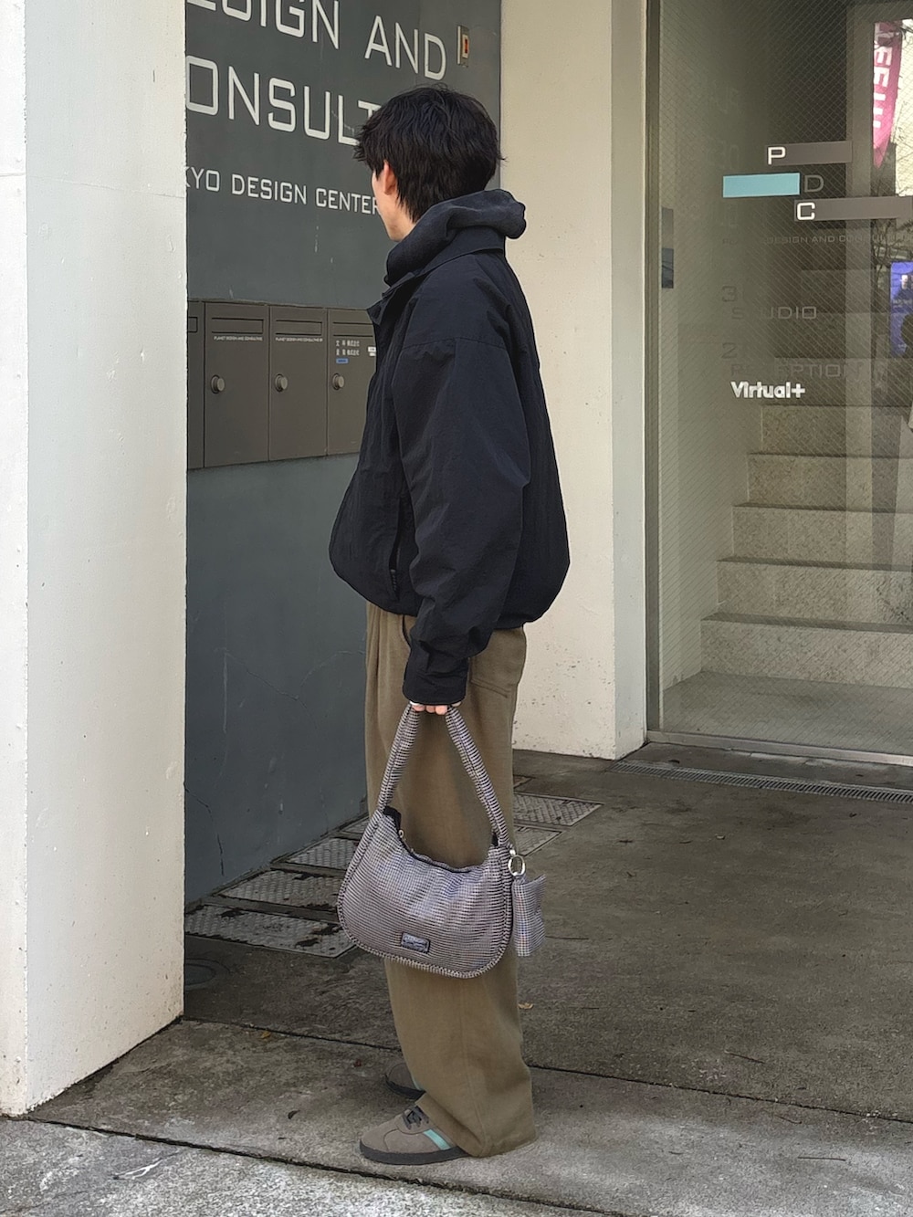 ブラック系のパーカー、ブラック系のナイロンジャケット、グリーン系のスラックスを着用したメンズの春コーディネートの2枚目の写真