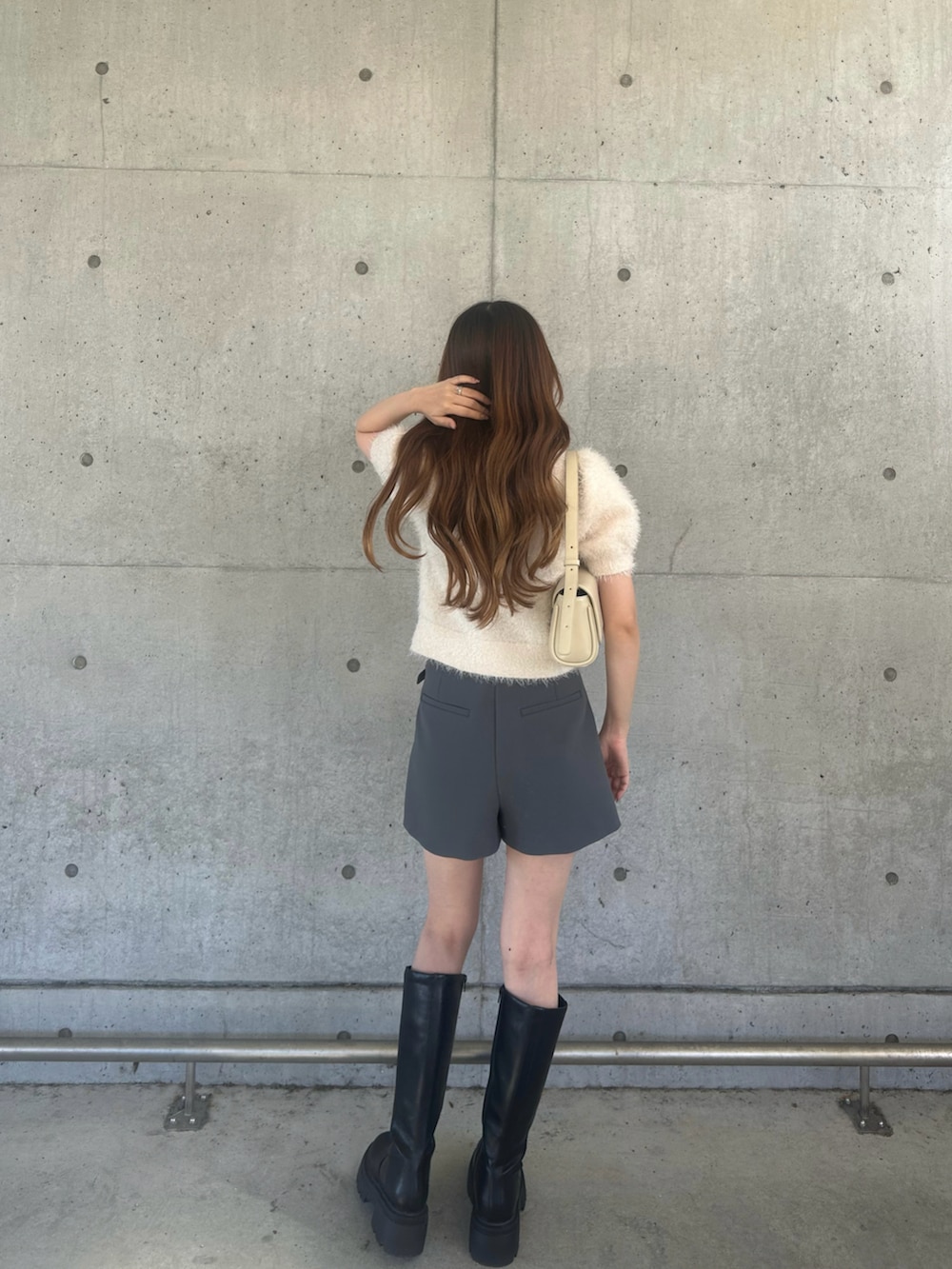 ブラック系のブーツ、グレー系のパンツ、ベージュ系のハンドバッグを着用したレディースの春コーディネートの2枚目の写真