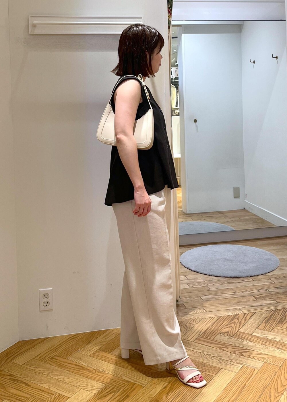 ホワイト系のハンドバッグ、ホワイト系のサンダル、ホワイト系のスラックスを着用したレディースの夏コーディネートの3枚目の写真