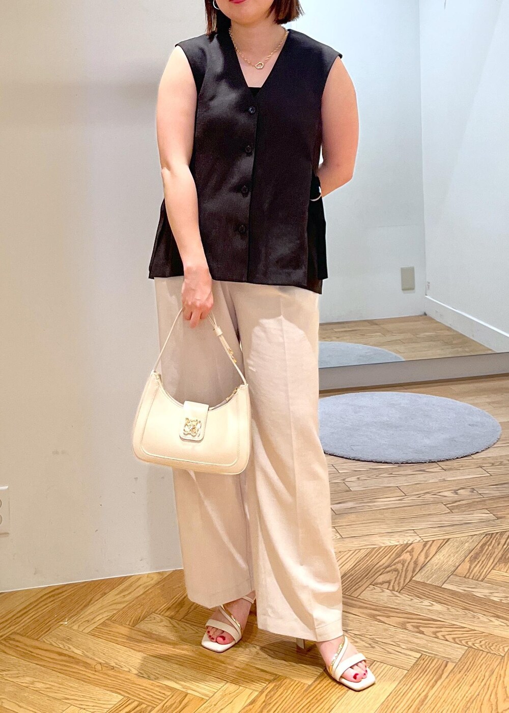 ホワイト系のハンドバッグ、ホワイト系のサンダル、ホワイト系のスラックスを着用したレディースの夏コーディネートの2枚目の写真