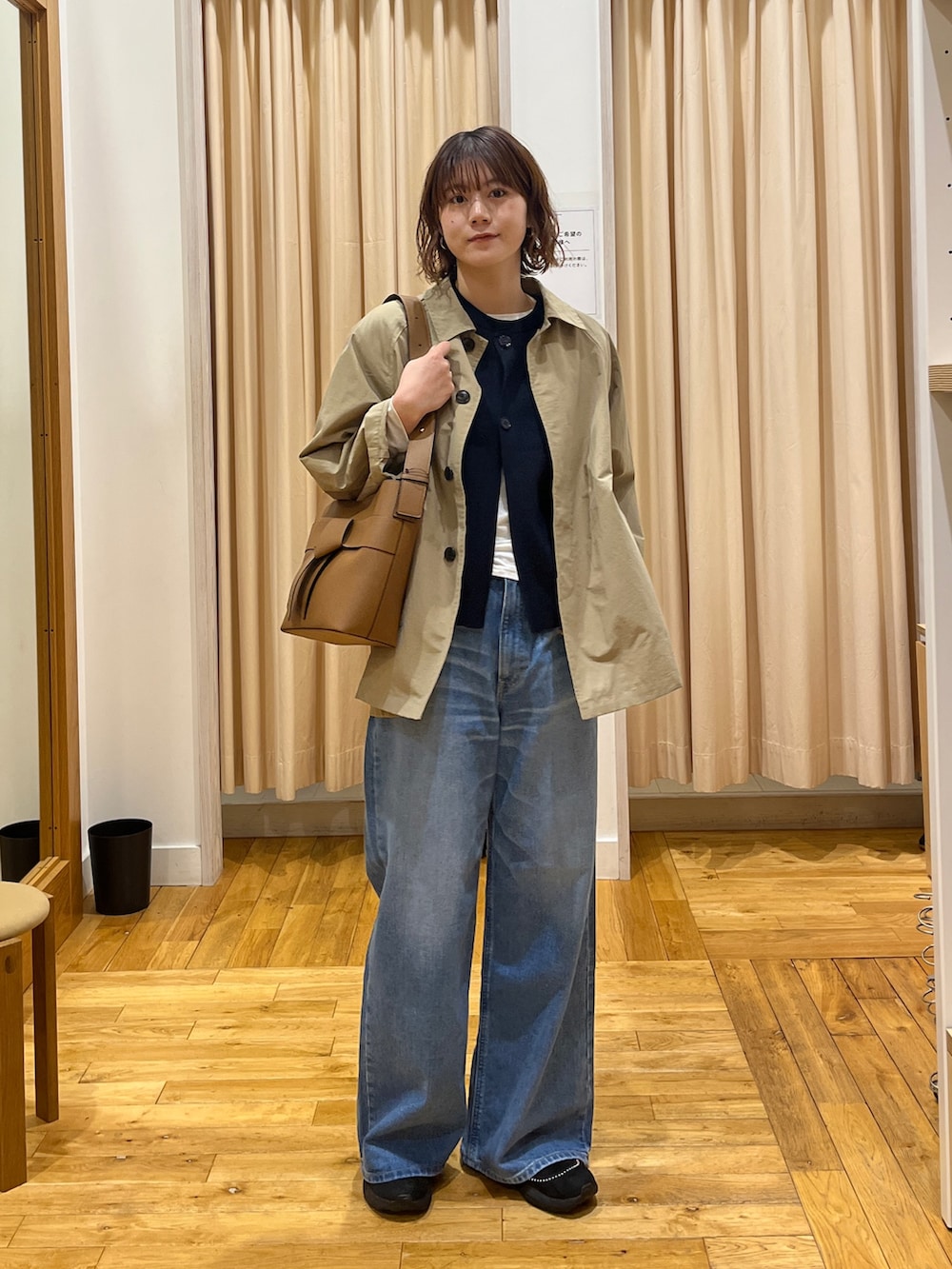 ベージュ系のステンカラーコート、ブルー系のベスト、ホワイト系のTシャツ/カットソーを着用したレディースの冬コーディネートの2枚目の写真