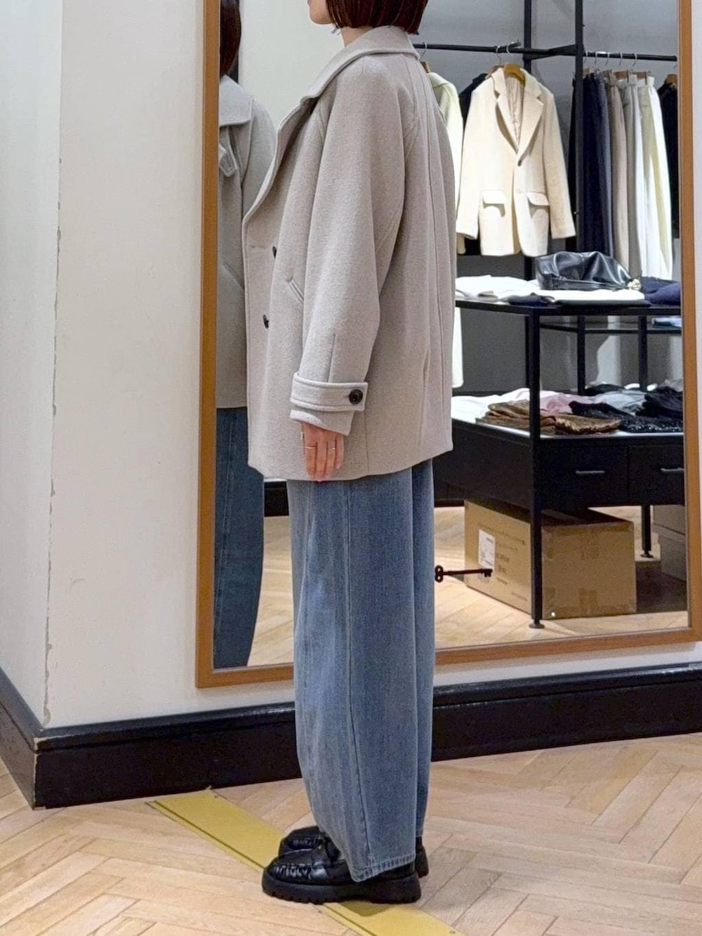 ベージュ系のピーコート、ブルー系のデニムパンツ、ブラック系のカーディガン/ボレロを着用したレディースの冬コーディネートの2枚目の写真