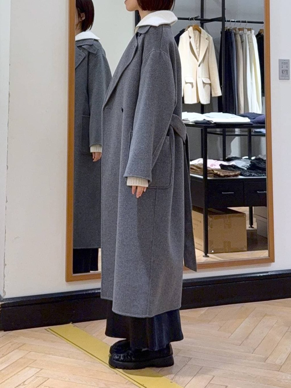 グレー系のステンカラーコート、ブルー系のスカート、ブラック系のショルダーバッグを着用したレディースの冬コーディネートの3枚目の写真