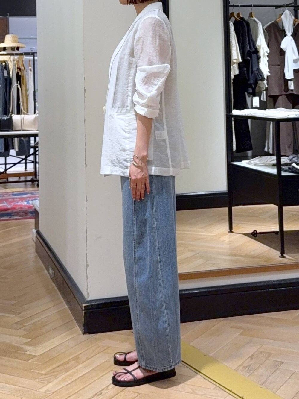 ブルー系のデニムパンツ、ホワイト系のテーラードジャケット、ブラック系のハンドバッグを着用したレディースの夏コーディネートの2枚目の写真