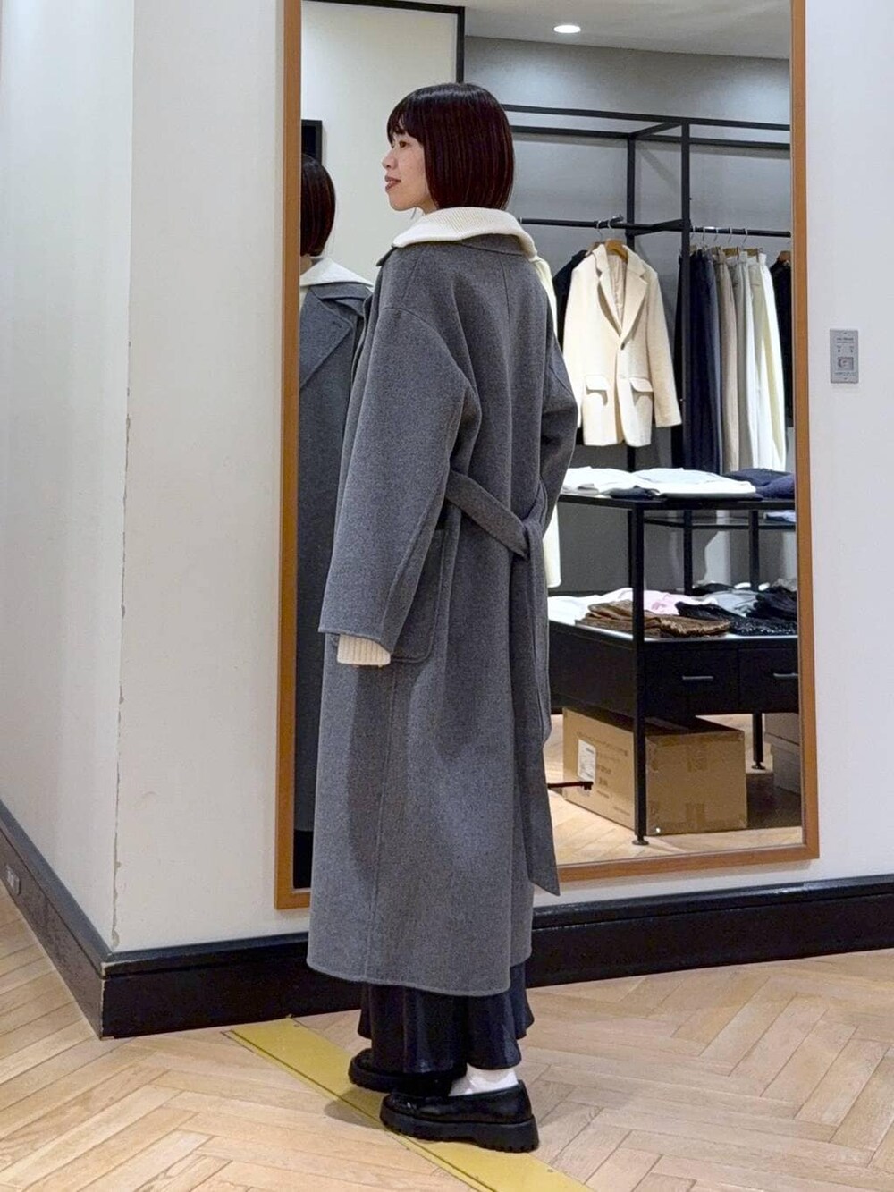 グレー系のステンカラーコート、ブルー系のスカート、ブラック系のショルダーバッグを着用したレディースの冬コーディネートの4枚目の写真