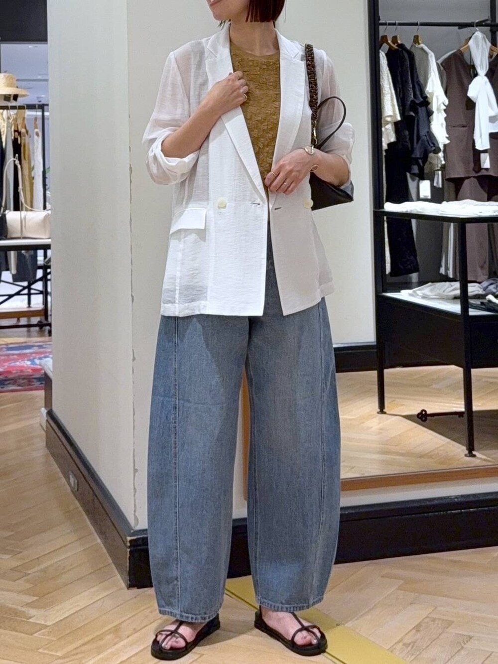 ブルー系のデニムパンツ、ホワイト系のテーラードジャケット、ブラック系のハンドバッグを着用したレディースの夏コーディネートの4枚目の写真