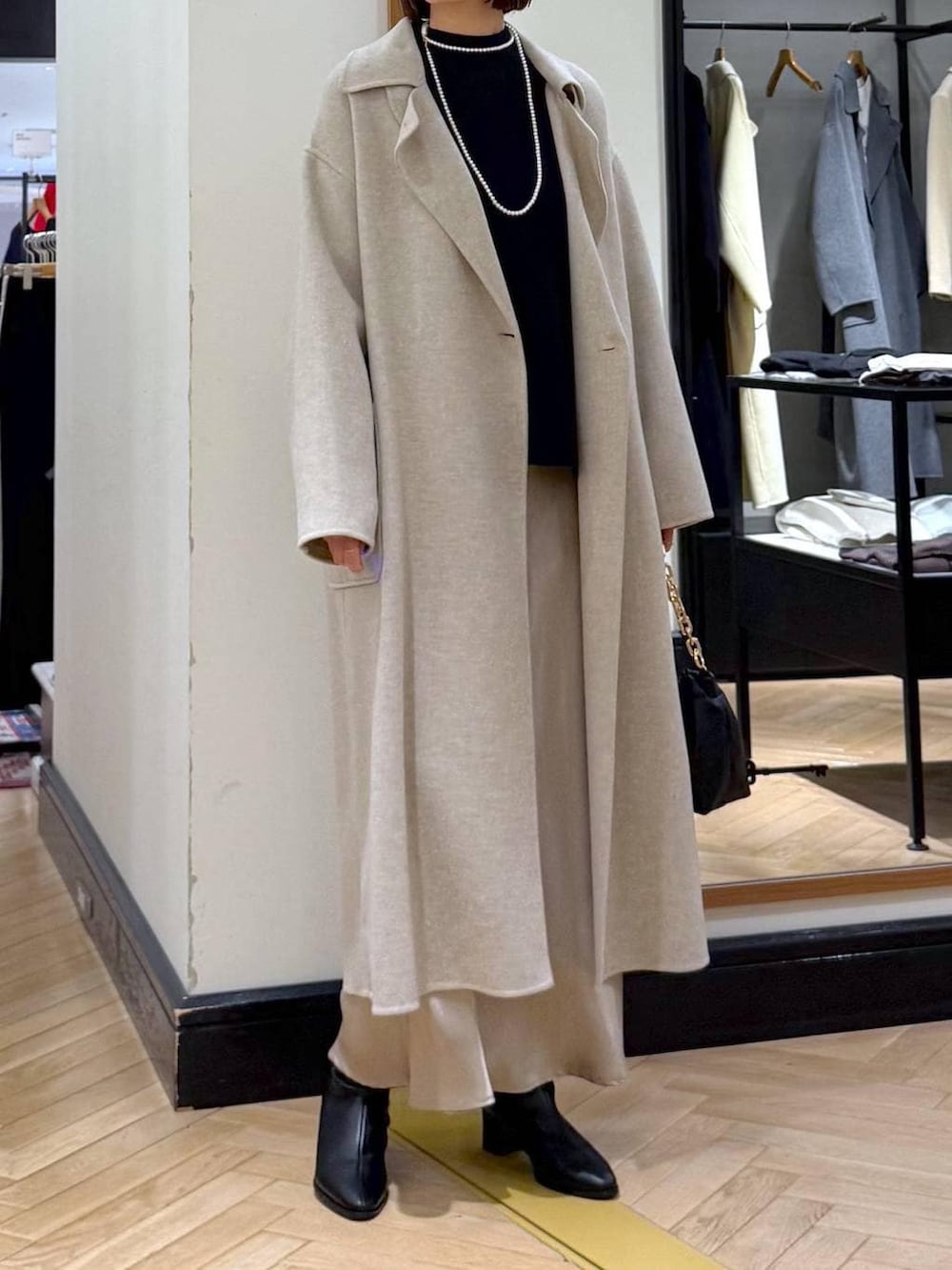 ベージュ系のステンカラーコート、ブラック系のブーツ、ブルー系のニット/セーターを着用したレディースの冬コーディネートの2枚目の写真