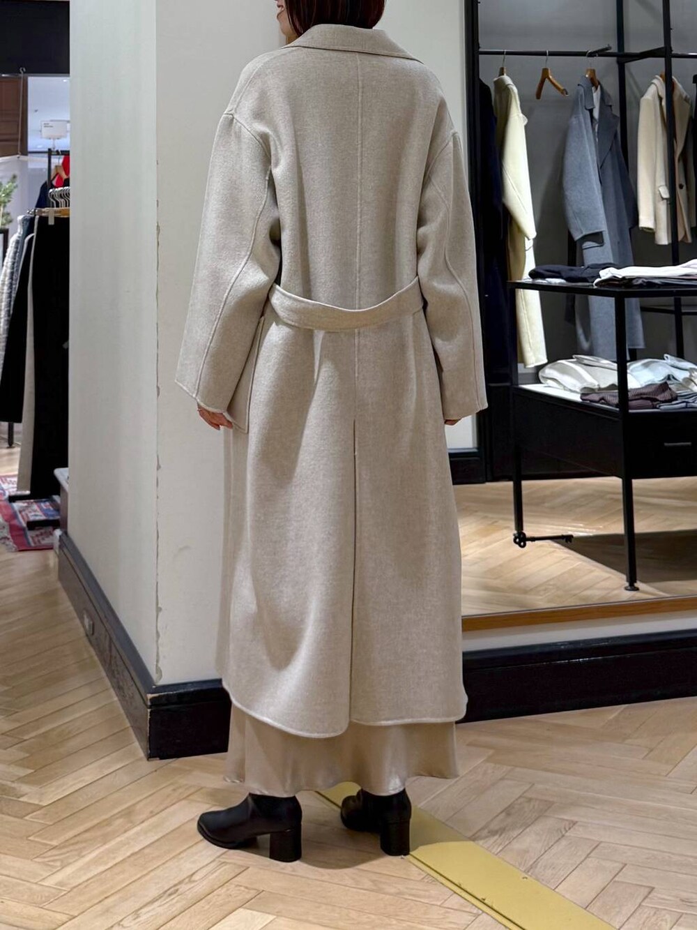 ベージュ系のステンカラーコート、ブラック系のブーツ、ブルー系のニット/セーターを着用したレディースの冬コーディネートの4枚目の写真