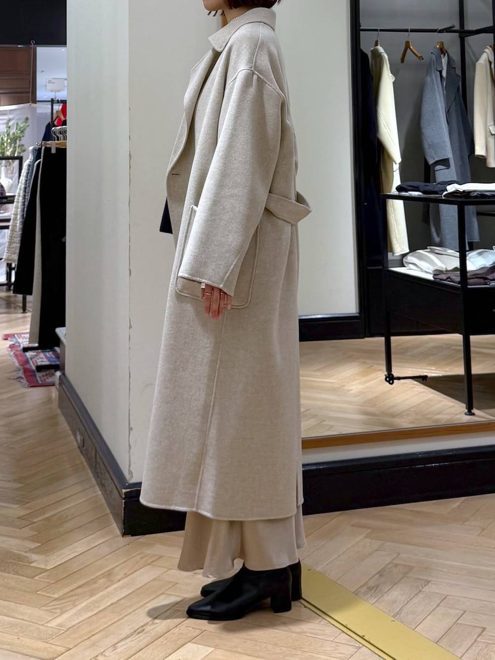 ベージュ系のステンカラーコート、ブラック系のブーツ、ブルー系のニット/セーターを着用したレディースの冬コーディネートの3枚目の写真