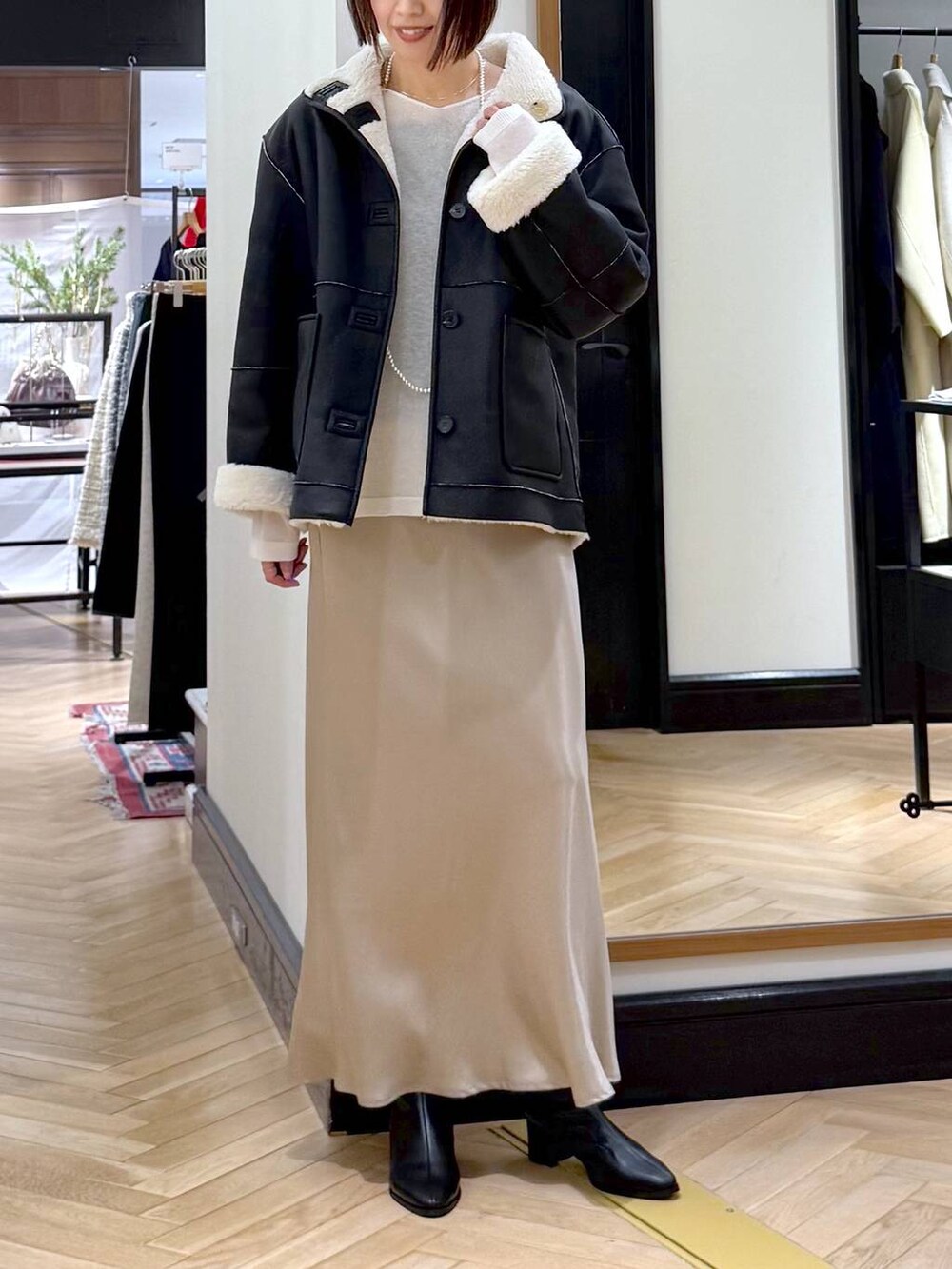 ブラック系のブーツ、ベージュ系のスカート、ブラック系のその他アウターを着用したレディースの冬コーディネートの2枚目の写真