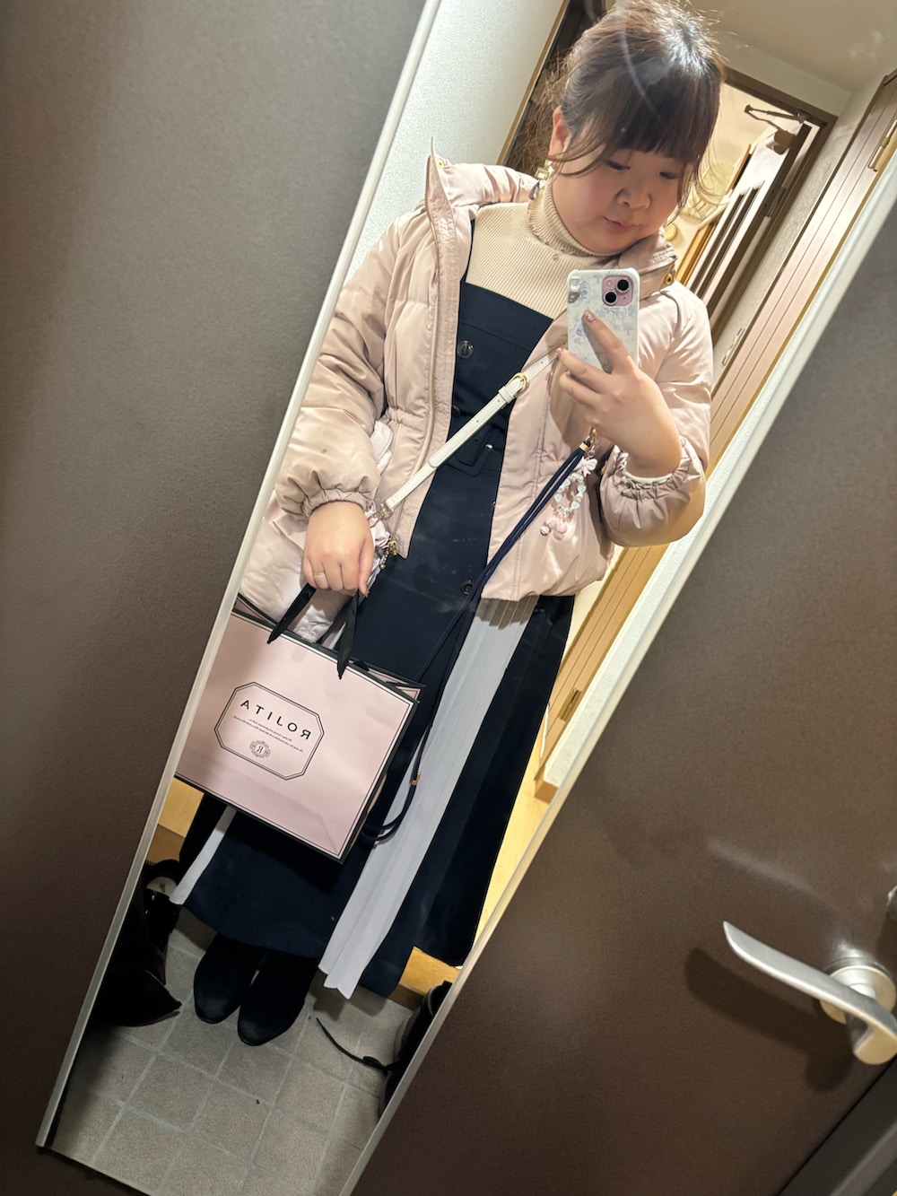 ピンク系のダウンジャケット/コート、ブルー系のジャンパースカート、ベージュ系のニット/セーターを着用したレディースの冬コーディネートの2枚目の写真