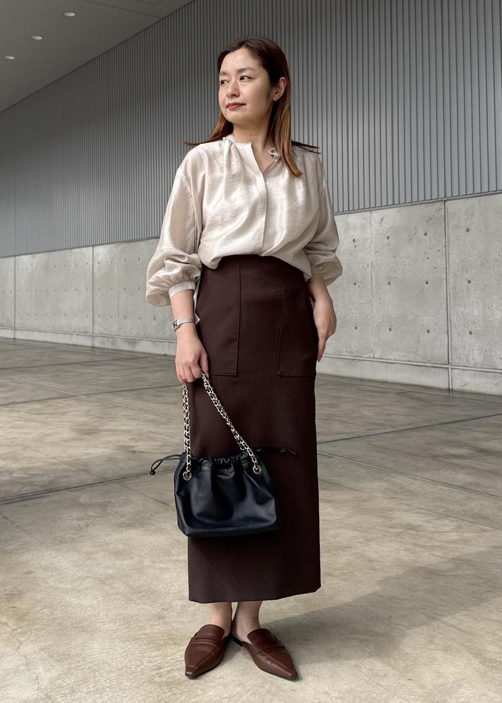 ブラック系のハンドバッグ、ブラウン系のスカート、ベージュ系のシャツ/ブラウスを着用したレディースの春コーディネートの6枚目の写真